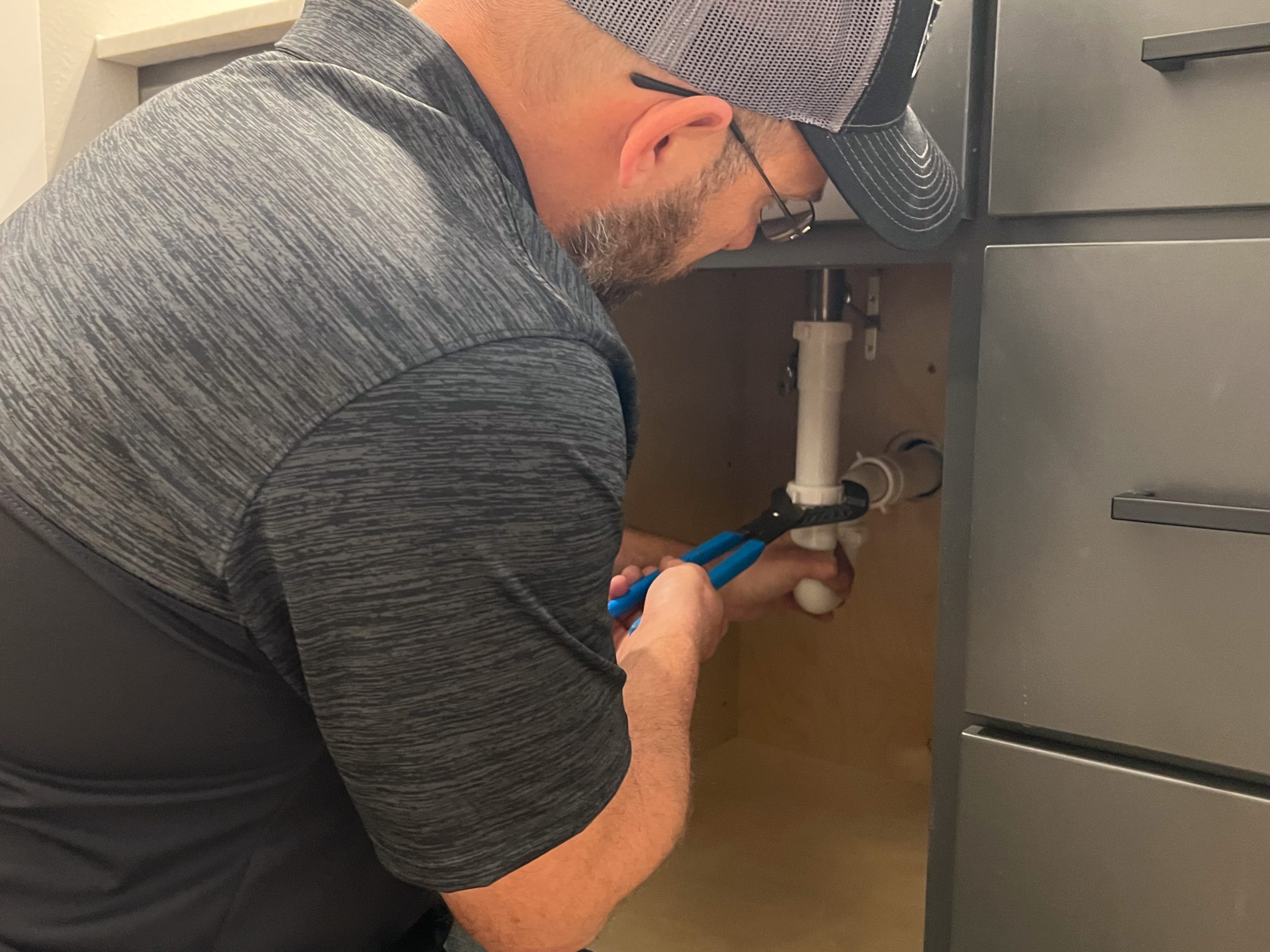 Schwickert's plumber tightening pipe underneath sink